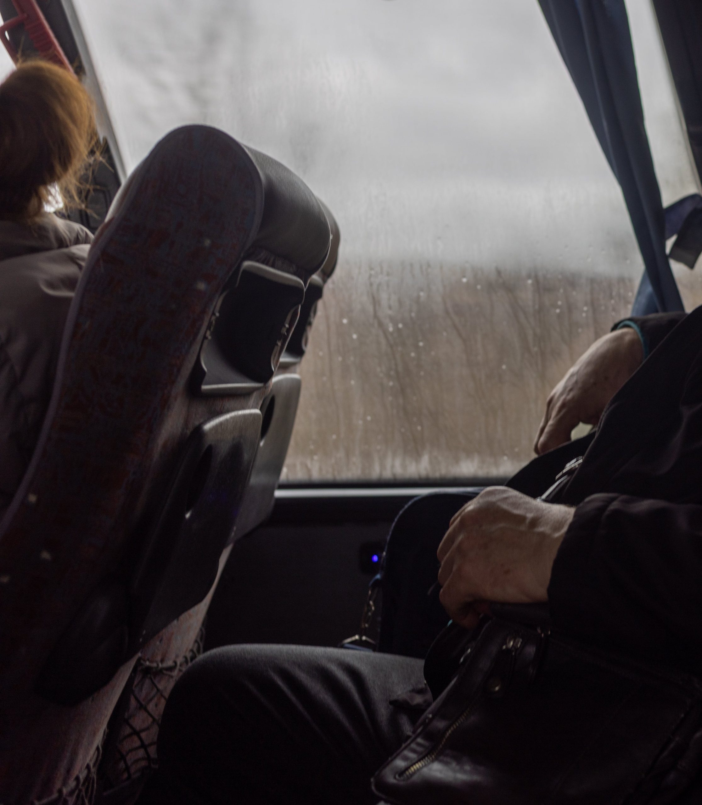 Photo prise à l'intérieur d'un car. Un homme occupe une place et devant une femme occupe une autre place.